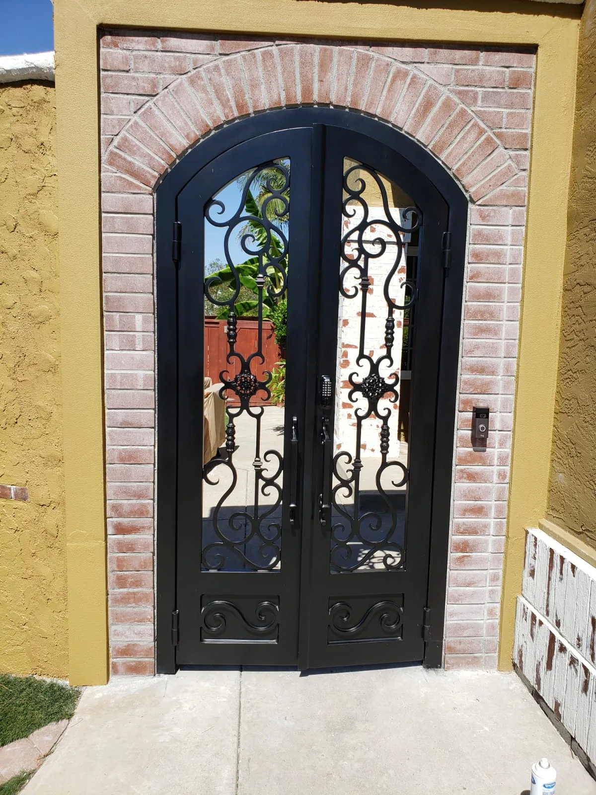 Arched black iron double entry doors in a brick archway