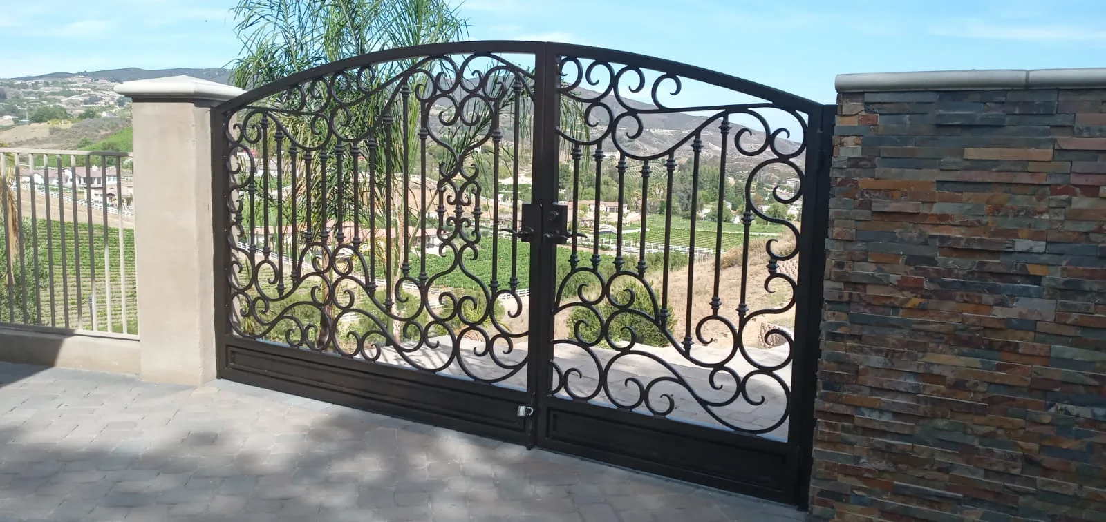 Wide bronze wrought iron driveway gate overlooking a hillside vineyard