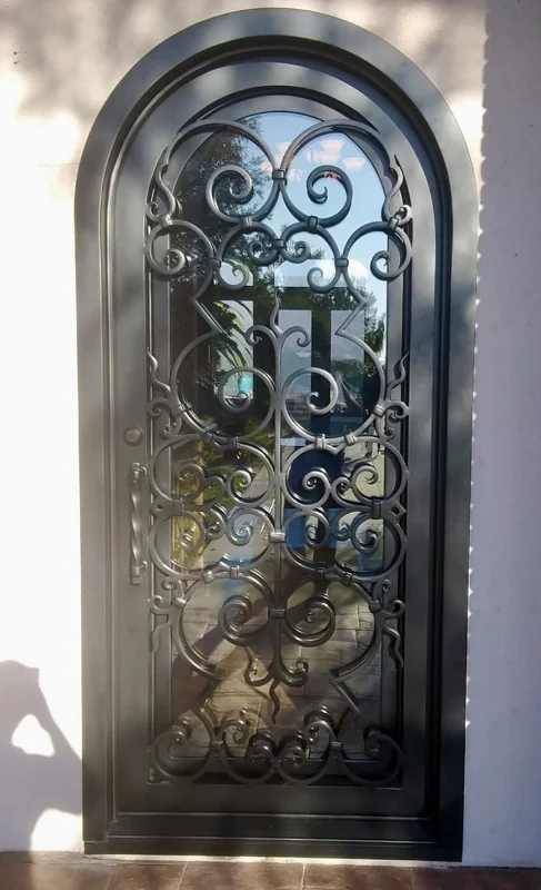 Tall arched iron door with dense symmetrical scrollwork