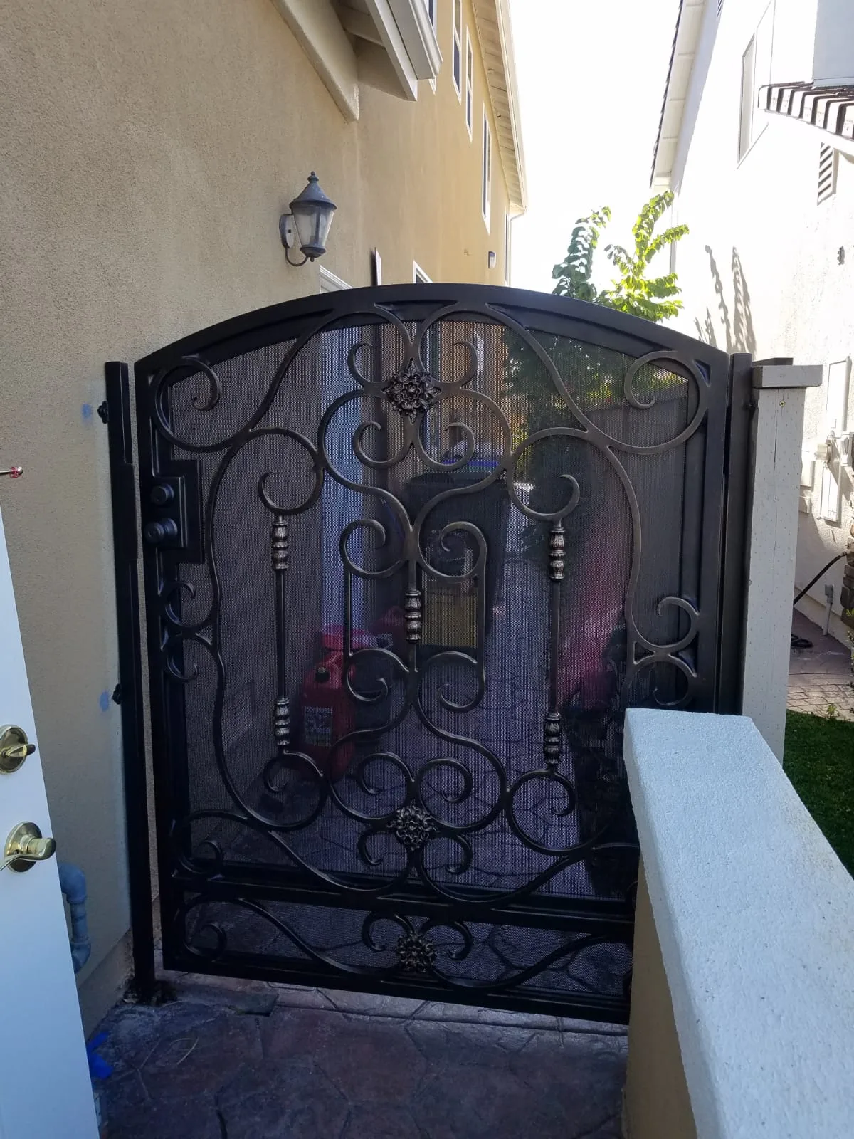 Arched wrought iron side yard gate with scrollwork and mesh backing