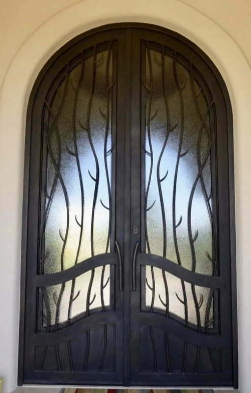 Arched double iron entry door with sculpted branch motif