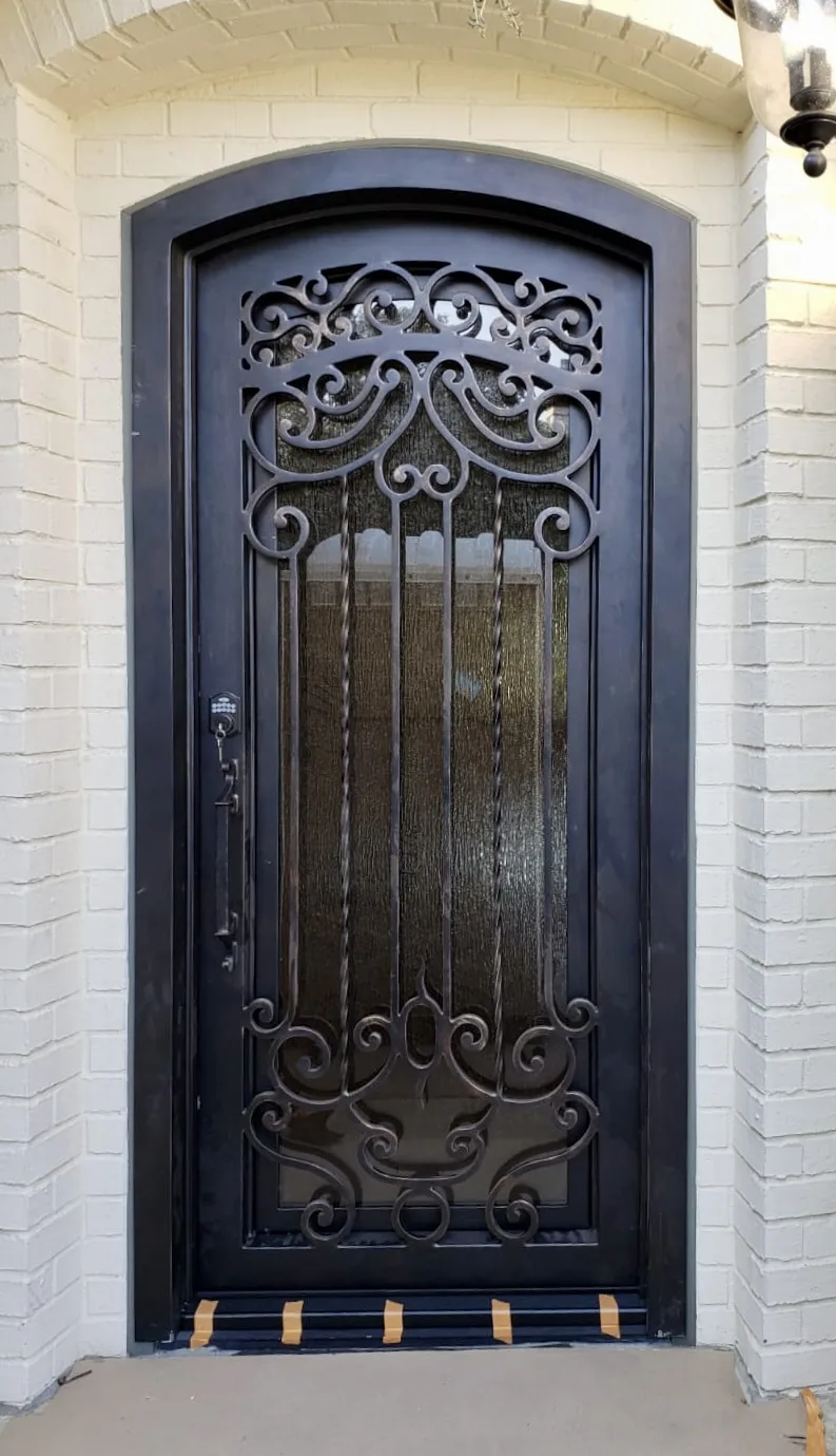 Arched iron entry door with ornate scrollwork against white brick